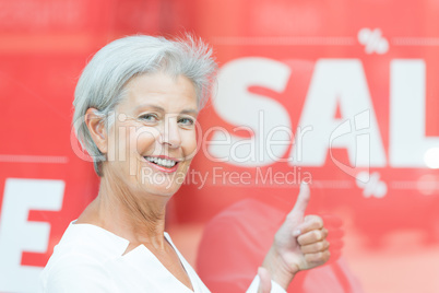 Seniorin vor einem Verkaufschild