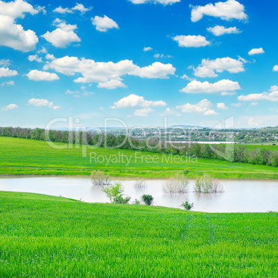 green field, lake and cloudy sky