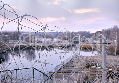 Post a fence of barbed wire in winter in frost at dawn