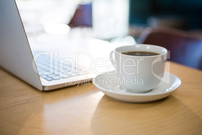 Close -up of cup of coffee and laptop on table