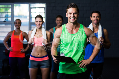 Smiling fitness instructor holding clipboard while people standing in background