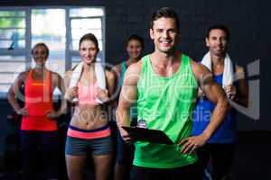Smiling fitness instructor holding clipboard while people standing in background
