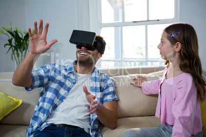 Father using virtual reality headset while daughter sitting beside him in the living room