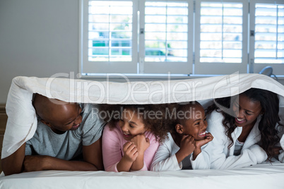 Happy family lying under a blanket on bed