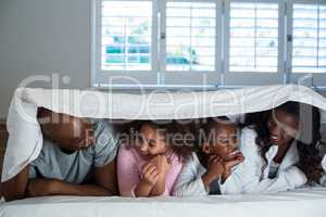 Happy family lying under a blanket on bed