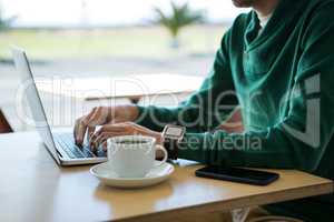 Man using laptop with coffee cup and mobile phone on table
