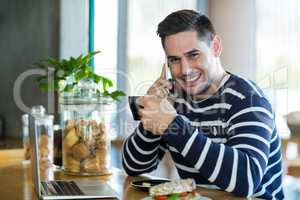 Smiling man talking on mobile phone while having coffee in cafÃ?Â©