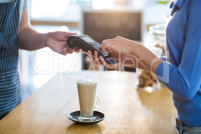 Customer making payment through payment terminal at counter in cafÃ?Â©