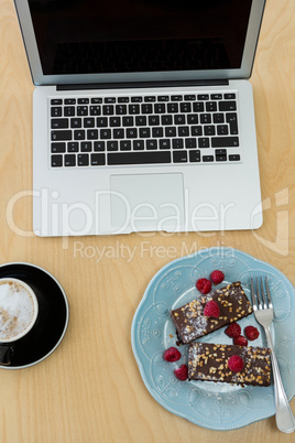 Delicious cakes, cup of coffee and laptop on table