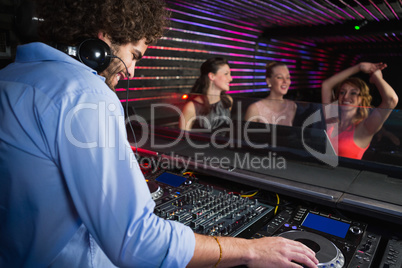 Male disc jockey playing music with three women dancing on the dance floor