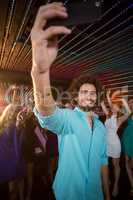 Man taking a selfie from mobile phone while friends dancing on dance floor