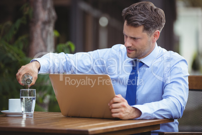 Handsome businessman pouring drink in glass while using laptop