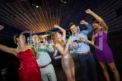 Smiling friends holding glasses of champagne and wine while dancing