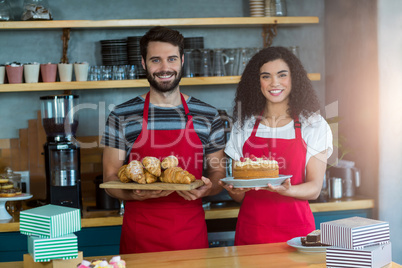 Portrait of waiter and waitress holding a tray of croissants and cake