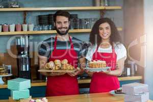 Portrait of waiter and waitress holding a tray of croissants and cake