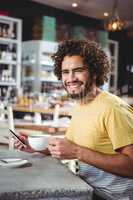 Man holding mobile phone while having coffee