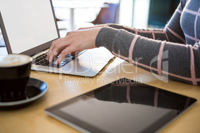 Woman using laptop with coffee and digital tablet on table