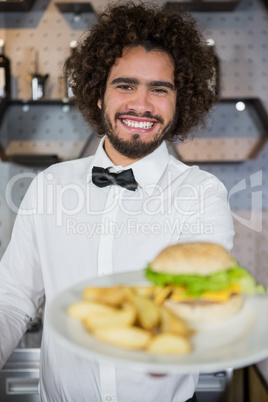 Waiter serving plates of potato chip and burger in bar