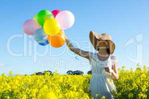 Woman holding colorful balloons in mustard field