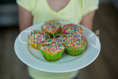 Mid-section of girl holding a plate of cupcakes