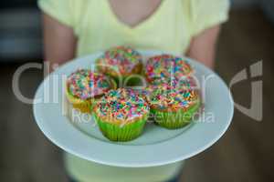 Mid-section of girl holding a plate of cupcakes