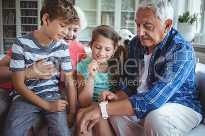 Grandparents and grandchildren looking at smartwatch in living room