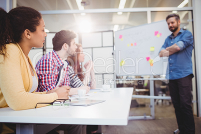 Executive standing in front of colleagues in meeting room at creative office