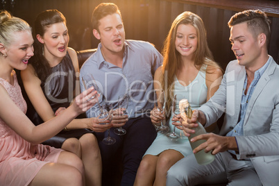 Man popping a champagne bottle while friends watching him