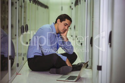 Stressed technician sitting on floor and looking at laptop