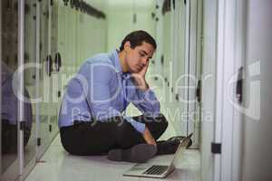 Stressed technician sitting on floor and looking at laptop