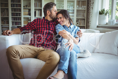 Man kissing woman while sitting on sofa in living room