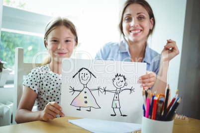 Mother and daughter sitting at table and daughter showing her drawing