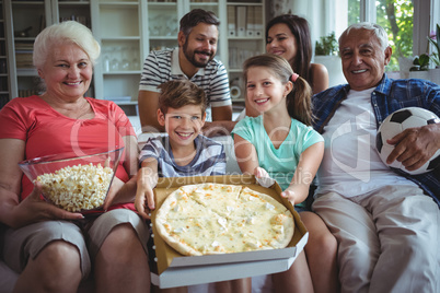 Multi-generation family sitting with popcorn and pizza while watching soccer match