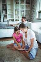 Mother and daughter sitting on floor and using digital tablet