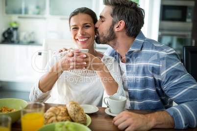 Man kissing on woman cheeks while having breakfast