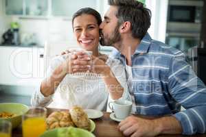 Man kissing on woman cheeks while having breakfast