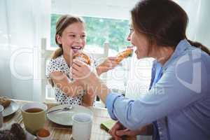 Mother and daughter feeding croissant to each other while having breakfast