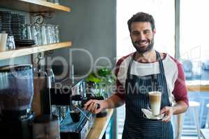 Smiling waiter holding cup of cold coffee at counter in cafe