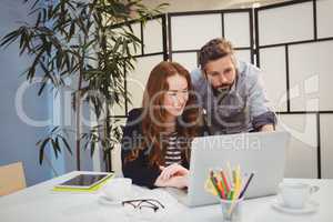 Confident colleagues using laptop at creative office