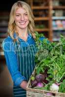 Smiling female staff holding a basket of fresh vegetables in organic section