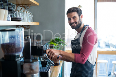 Smiling waiter making cup of coffee at counter in cafe