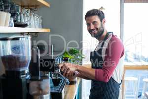 Smiling waiter making cup of coffee at counter in cafe