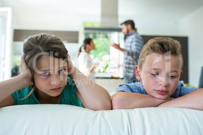 Sad kids leaning on sofa while parents arguing in background