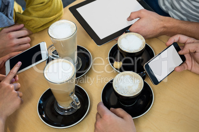 Friends using mobile phone and digital tablet while having cup of coffee