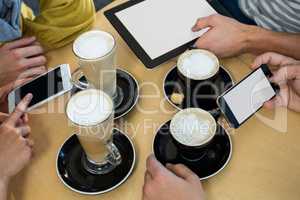 Friends using mobile phone and digital tablet while having cup of coffee