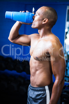Shirtless man drinking water in gym