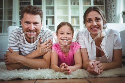 Happy parents and daughter lying on rug in living room