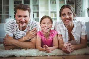 Happy parents and daughter lying on rug in living room