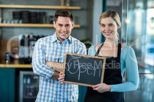Waitress and man standing with open sign on slate in cafe