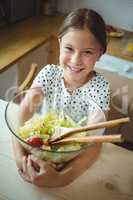 Girl holding a bowl of salad in kitchen